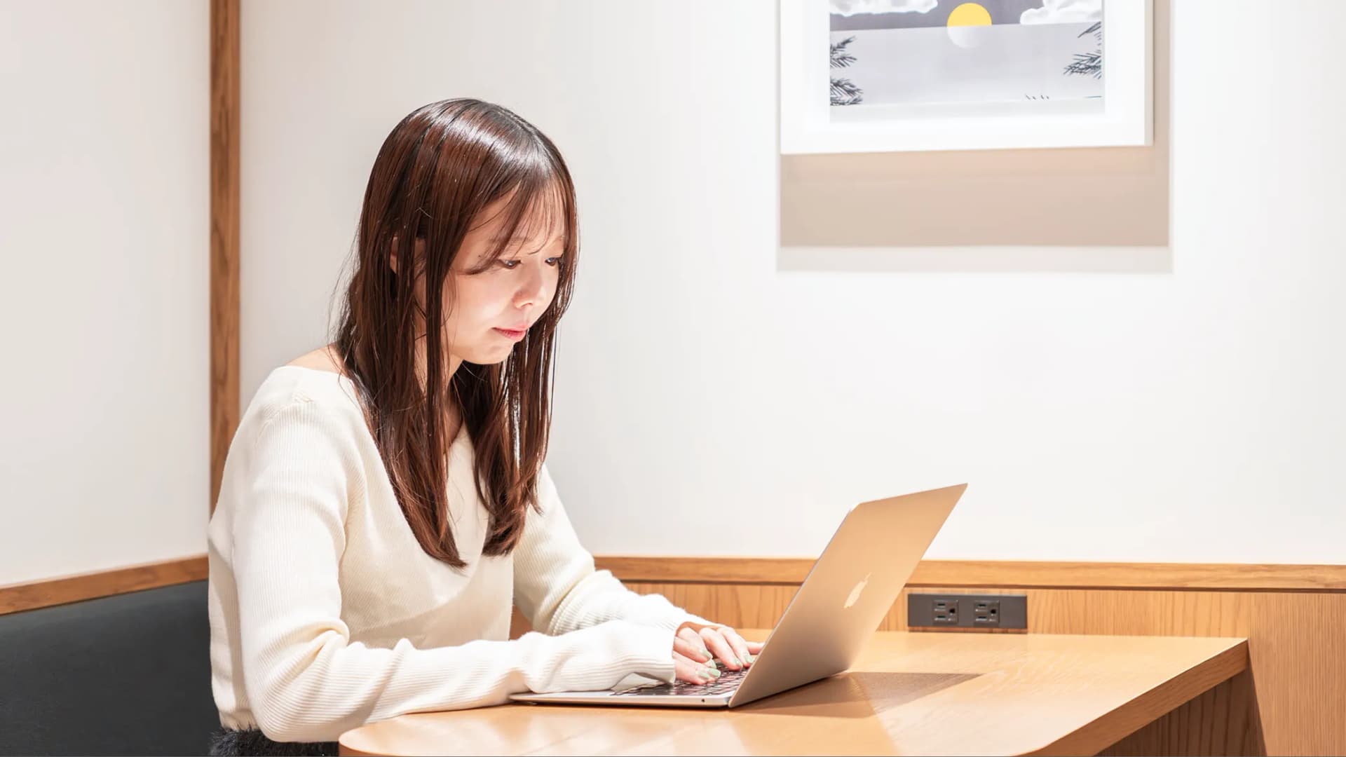 写真。女性がテーブルでMacBookを開いて作業している様子