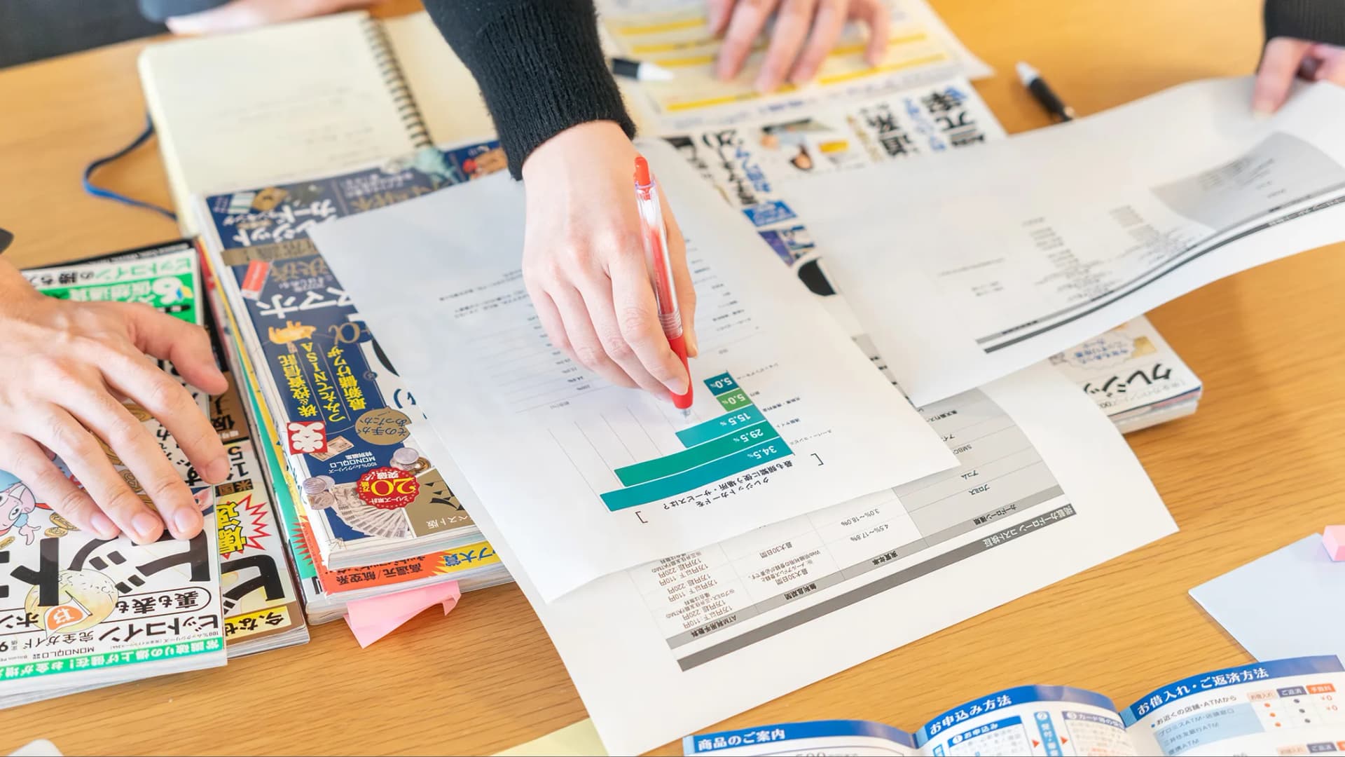 写真。雑誌の上で評価項目の書かれた紙に赤ペンで修正を入れたり書き込んだりしている様子